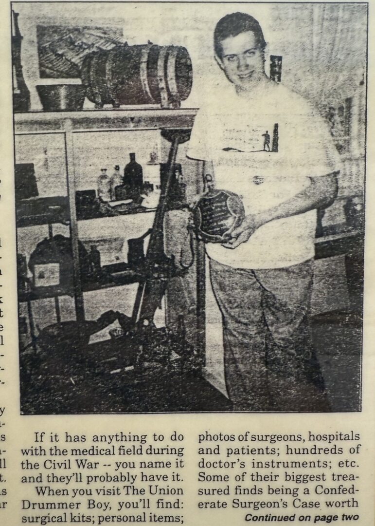 A person stands in a room filled with Civil War medical artifacts, holding a drum, next to shelves with various historical items and equipment.