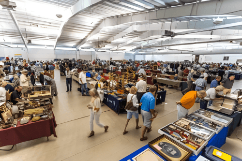 People browsing tables with antiques and collectibles at a large indoor market.